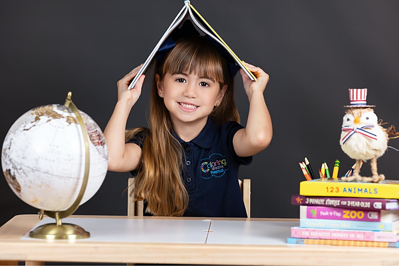 Niña jugando con un libro sobre la cabeza, junto a un globo terráqueo